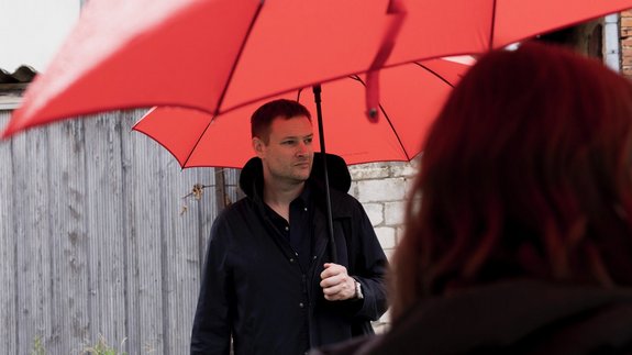 Künstler Simon Denny unter einem Regenschirm