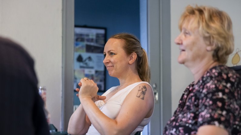 Two women are sitting next to each other at a table. They are looking in the same direction and laughing.