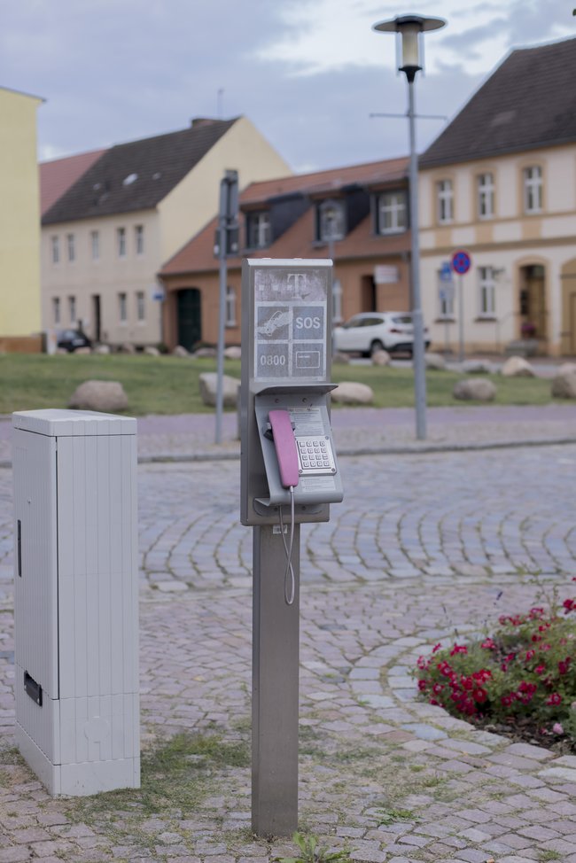 Altes öffentliches Telefon mit SOS-Zeichen steht in menschenleerem dörflichem Umfeld