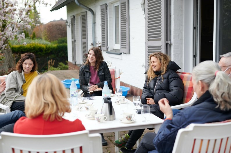 Künstlerin Kerstin Brätsch sitzt mit der Auftraggebergruppe von Wickrath an einem Gartentisch