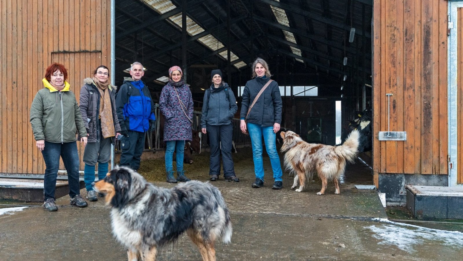 Group of The New Patrons of Waldeck-Frankenberg and two dogs stand at the entrance gate of a farm building.