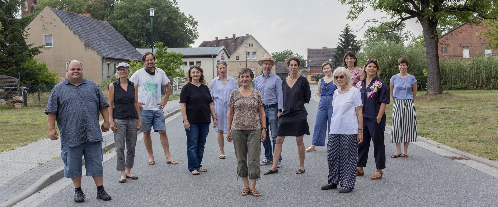 Menschen stehen auf einer Dorfstraße und schauen den Betrachter an