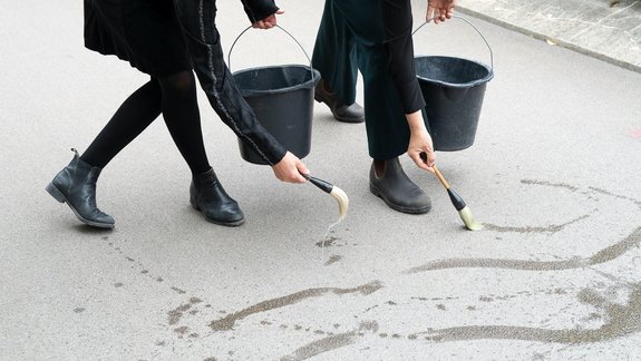 Detail of a picture, the hands of two people painting with brushes on asphalt
