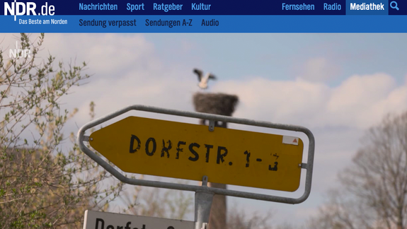 Bildausschnitt des NDR Kulturjournal mit einem Straßenschild mit Namen Dorfstraße