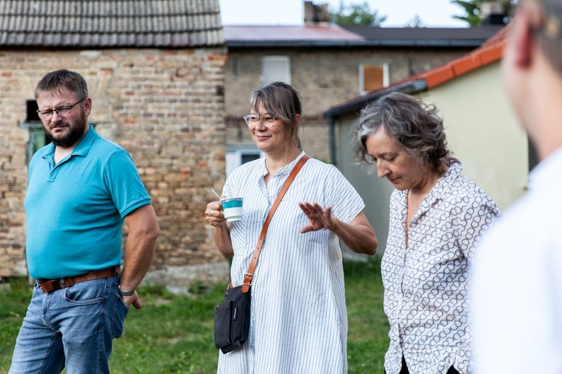 Künstlerin Antje Majewski, Mediatorin Susanne Burmester und zwei weitere Personen stehen in einem Garten beim Besuch in Wietstock