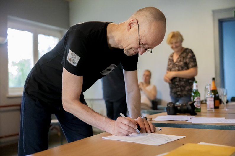 A man signs a paper on a wooden table