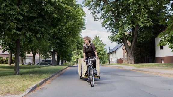 Eine Person der Neuen Auftraggeber ist mit dem Fahrrad im Dorf unterwegs
